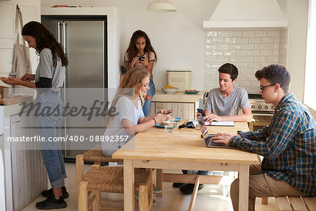Teenage friends in kitchen, doing homework and making food