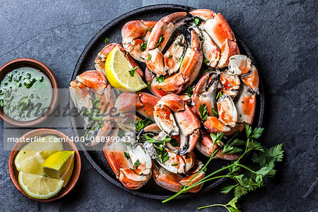 Seafood. Crabs tentacles on black plate with wite wine, lemon and herbs sauce on slate background. Top view