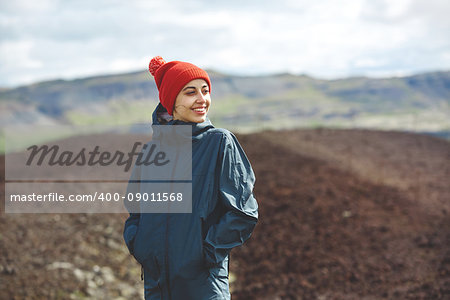 Girl in warm clothing observing surroundings on background of mountains of Iceland.
