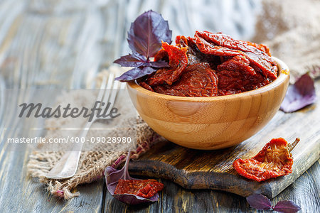 Bowl with sun-dried tomatoes, purple basil and fork on wooden table,selective focus.