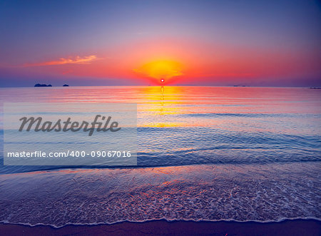 Beautiful tropical sunset in Krabi, Thailand. Dramatic and picturesque evening scene. Ocean waves and colorful cloudy sky and sun in the background. Nature landscape. Travel background. Bright colors