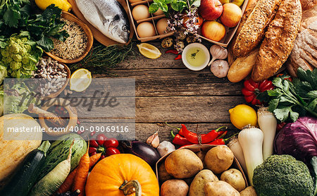 Different foods on a wooden background wiht copyspace. Various fruits and vegetables, fish, bread and eggs.