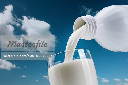 Pouring fresh milk from a bottle into a glass, blue sky with clouds on the background