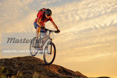 Cyclist in Red T-Shirt Riding the Bike Down the Rock on the Sunset Sky Background. Extreme Sport and Enduro Biking Concept.