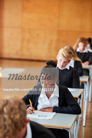 Teenage Students In Uniform Sitting Examination In School Hall