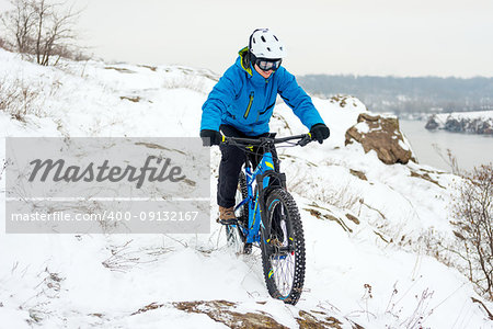 Cyclist in Blue Riding the Mountain Bike on the Rocky Winter Hill Covered with Snow. Extreme Sport and Enduro Biking Concept.