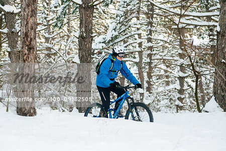 Cyclist in Blue Riding the Mountain Bike in the Beautiful Winter Forest Covered with Snow. Extreme Sport and Enduro Biking Concept.