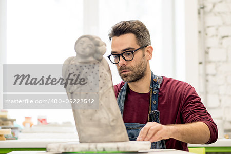 Portrait of Ceramist Dressed in an Apron Working on Clay Sculpture in the Bright Ceramic Workshop.