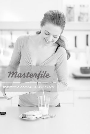 Happy young woman pouring milk into glass