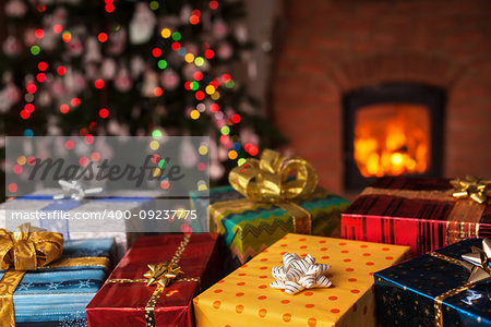 Many christmas presents in front of xmas tree and fireplace in a dark room