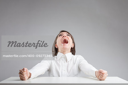 high pressure with anger and stress concept, in a portrait of a woman on a gray background that's shouting to the sky with her punches clenched