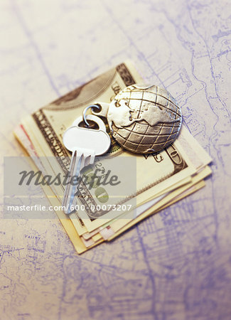 Key with Globe Keychain on Stack Of Currency on Map