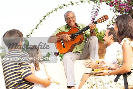 Family Sitting Outdoors Listening to Man Playing Guitar