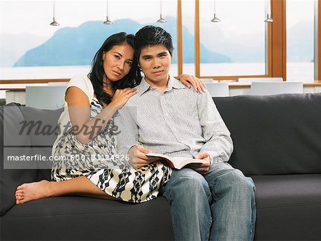 Couple Sitting on Sofa Reading Book Together