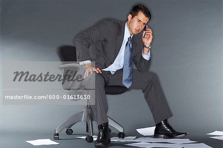 Angry Businessman Talking on Cell Phone Surrounded by Documents