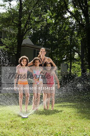 Portrait of Mother with Children Playing in Backyard with Sprinkler