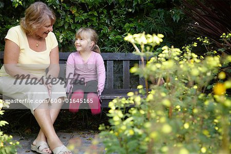 Grandmother and Granddaughter Sitting on Bench in Garden