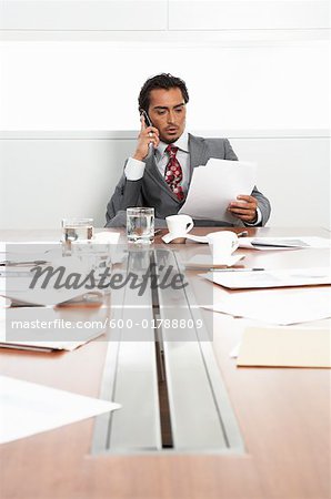 Businessman at Boardroom Table with Cellular Phone and Documents