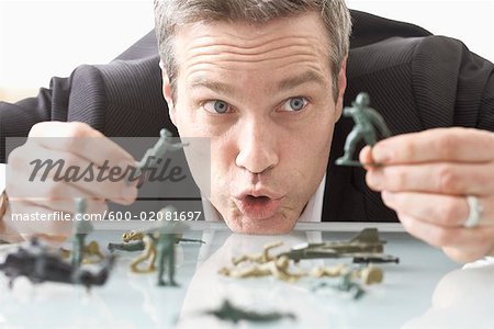 Businessman Playing with Toy Soldiers on Desk