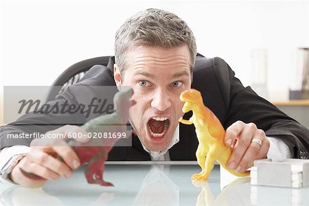 Businessman Playing with Toy Dinosaurs on Desk Stock Photo