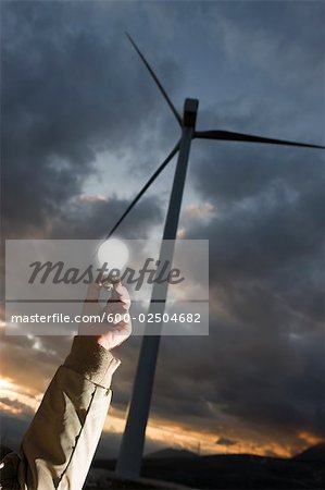 Man Holding Lightbulb by Wind Turbine