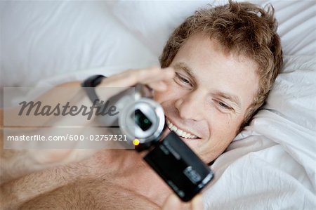 Man Lying in Bed Holding a Video Camera