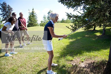 Group of Golfers Watching Woman Try to Retrieve Golf Ball From a Tree