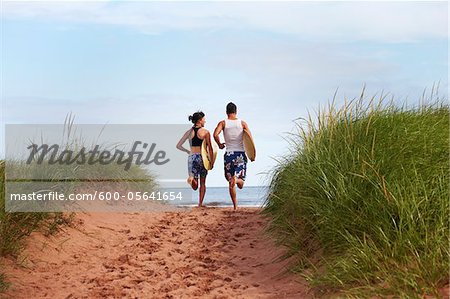 Young Woman and Young Man holding Skimboards while Running to Beach, PEI, Canada