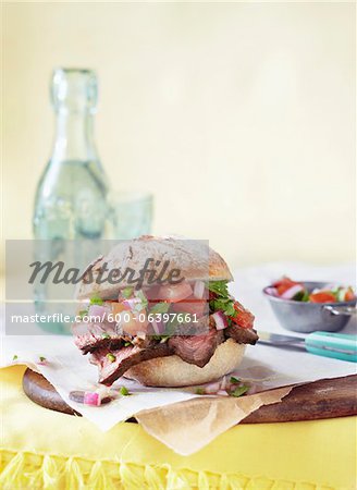 Steak Sandwich on Bun With Tomatoes and Onions on Table