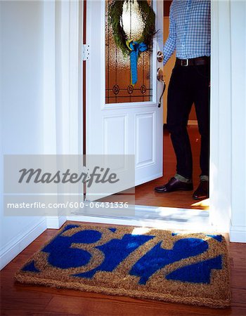 https://image1.masterfile.com/getImage/600-06431336em-man-opening-door-to-home-with-welcome-mat-with-house-number-and.jpg