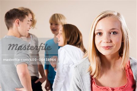 Portrait of Blond, Teenage Girl Smiling at Camera with Group of Teenage Boys and Girls Talking in Background, Studio Shot on White Background