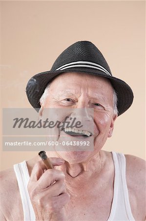 Close-up Portrait of Senior Man wearing Undershirt and Hat while Smoking a Cigar and Smiling, Studio Shot on Beige Background