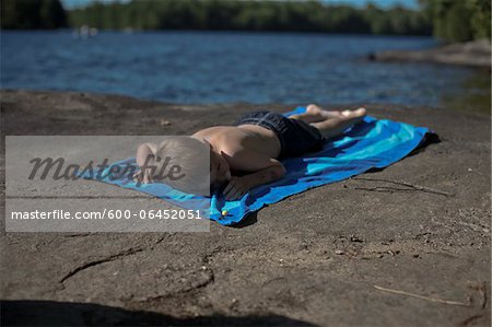 Boy Lying on Beach Towel on Rocks by Lake, Muskoka, Ontario, Canada