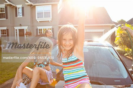 A family washes their car in the driveway of their home on a sunny summer afternoon in Portland, Oregon, USA