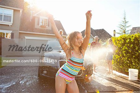 Young girl dances while family washes car in the driveway of their home on a sunny summer afternoon in Portland, Oregon, USA