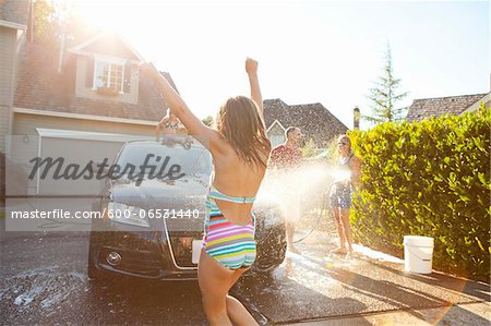 Young girl dances while family washes their car in the driveway of their home on a sunny summer afternoon in Portland, Oregon, USA