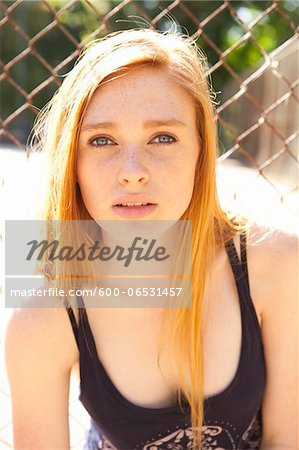 Close-up portrait of young woman standing in front of chain link fence in park near the tennis court on a warm summer day in Portland, Oregon, USA