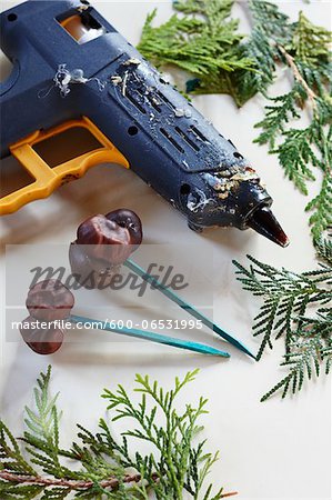 Glue gun on a craft table with cedar branches and chestnuts glued as a holiday craft