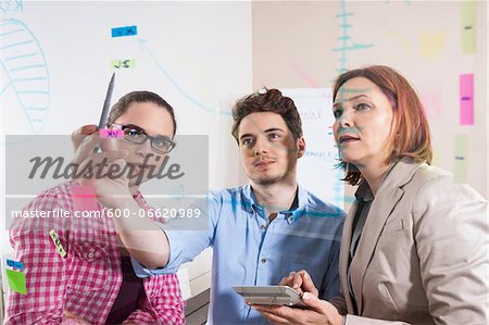 Business People Working in Office Looking at Plans Displayed on a Glass Board