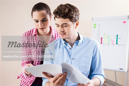 Young Businessman and Young Businesswoman Reading Document in Office