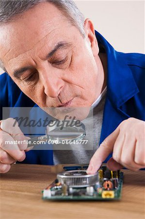 Man Looking at Circuit Board with Magnifying Glass in Studio