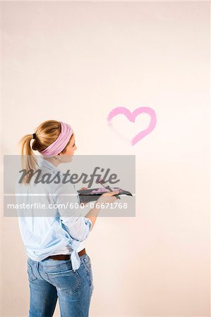 Studio Shot of Young Woman Painting Heart on Wall