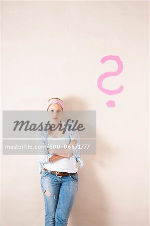 Studio Shot of Young Woman Leaning Against Wall with Question Mark