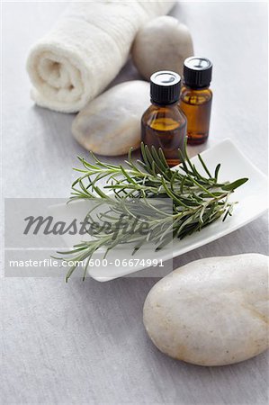 Sprig of rosemary, fresh herbs, a towel and bottles of essential oil for aromatherapy