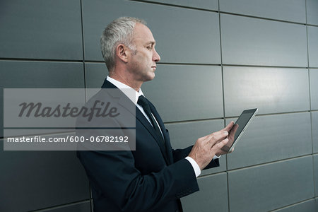 Mature businessman standing in front of wall, looking at tablet computer