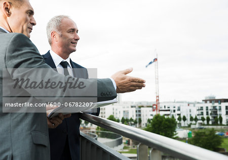 Mature businessmen standing on outdoor balcony, talking and overlooking city, Mannheim, Germany