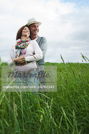 Portrait of mature couple standing in field of grass, embracing, Germany