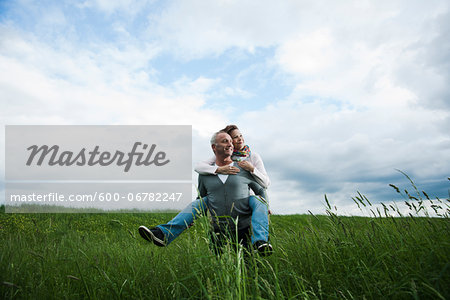 Mature couple in field of grass, man giving piggyback ride to woman, Germany