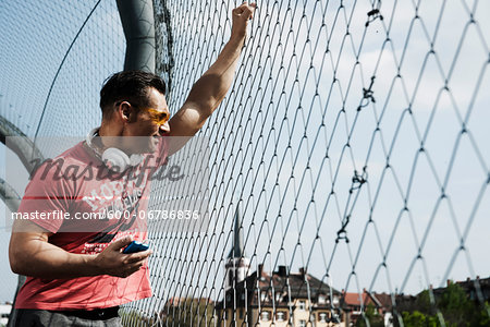 Mature man standing on outdoor basketball court holding MP3 player, Germany