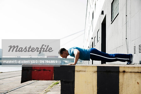 Mature man doing push-ups outdoors, on loading dock in front of warehouse, Mannheim, Germany